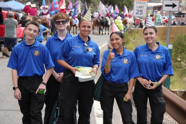 Five Explorers smile on the parade route carrying 'My Visit with the Sheriff' activity books and wristbands