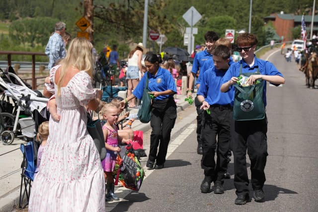 Explorers walk a parade route handing items to children seated along the curb