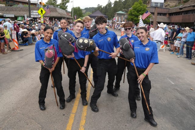 Seven Explorers pose playfully with sheriff-badged stick horses in the middle of the parade route