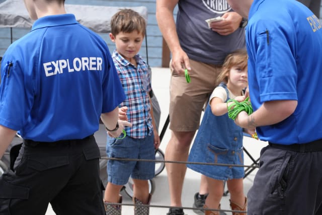Two Explorers hand green 'Join the JCSO' wristbands to young children at an event table
