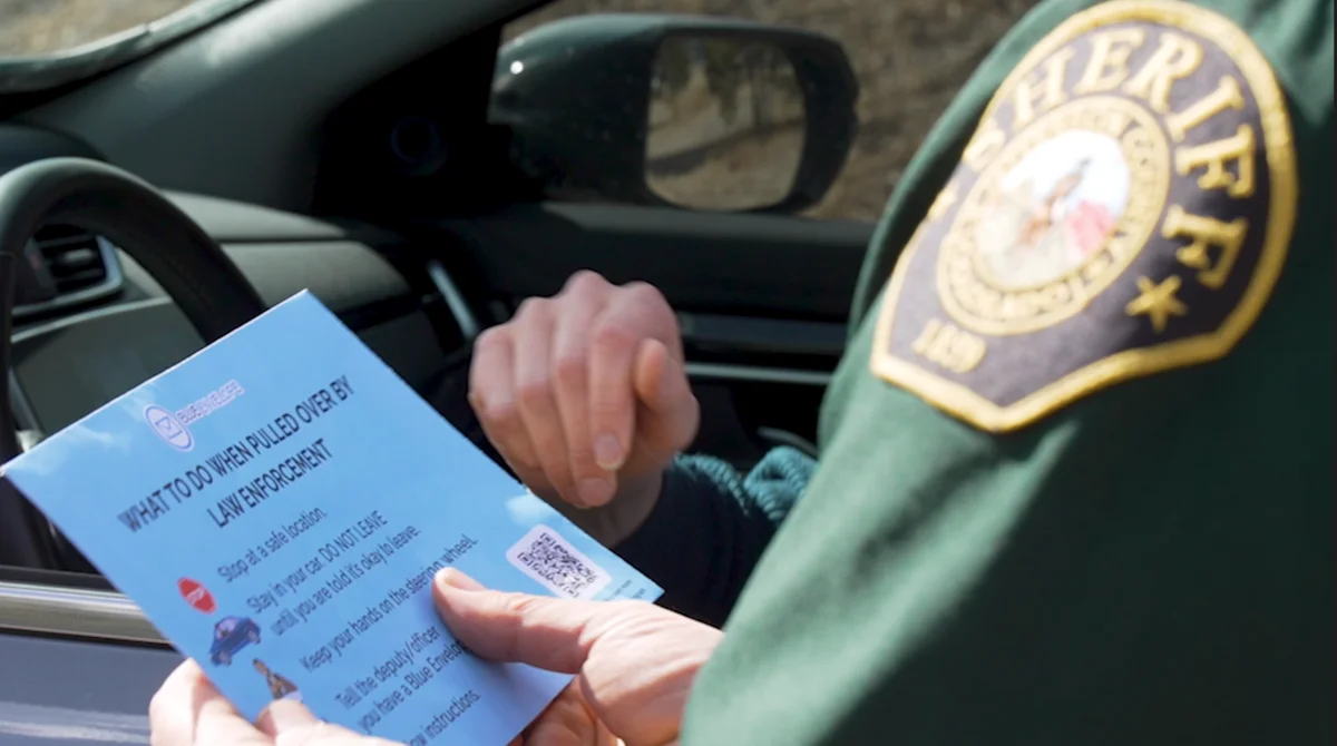 Sheriff's deputy reading a Blue Envelope card while speaking with a driver at a traffic stop