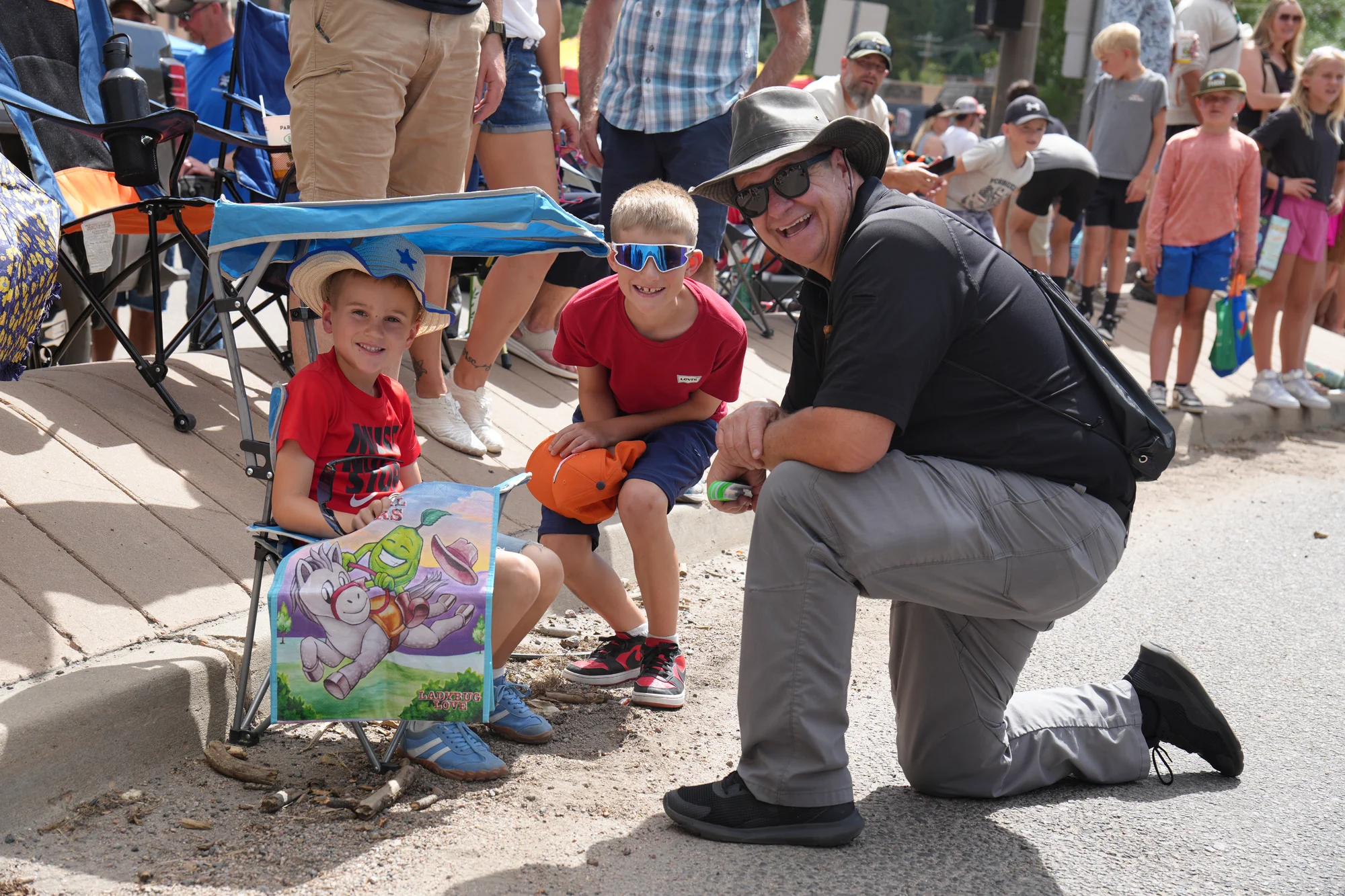 Community Resource Deputy Mark Bybee kneeling with two smiling young parade-goers along the curb at the Evergreen Parade and Rodeo