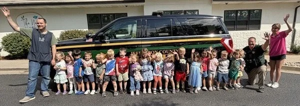 Deputy Bybee and Nest Schools of Ken Caryl students waving beside his patrol car during a June visit