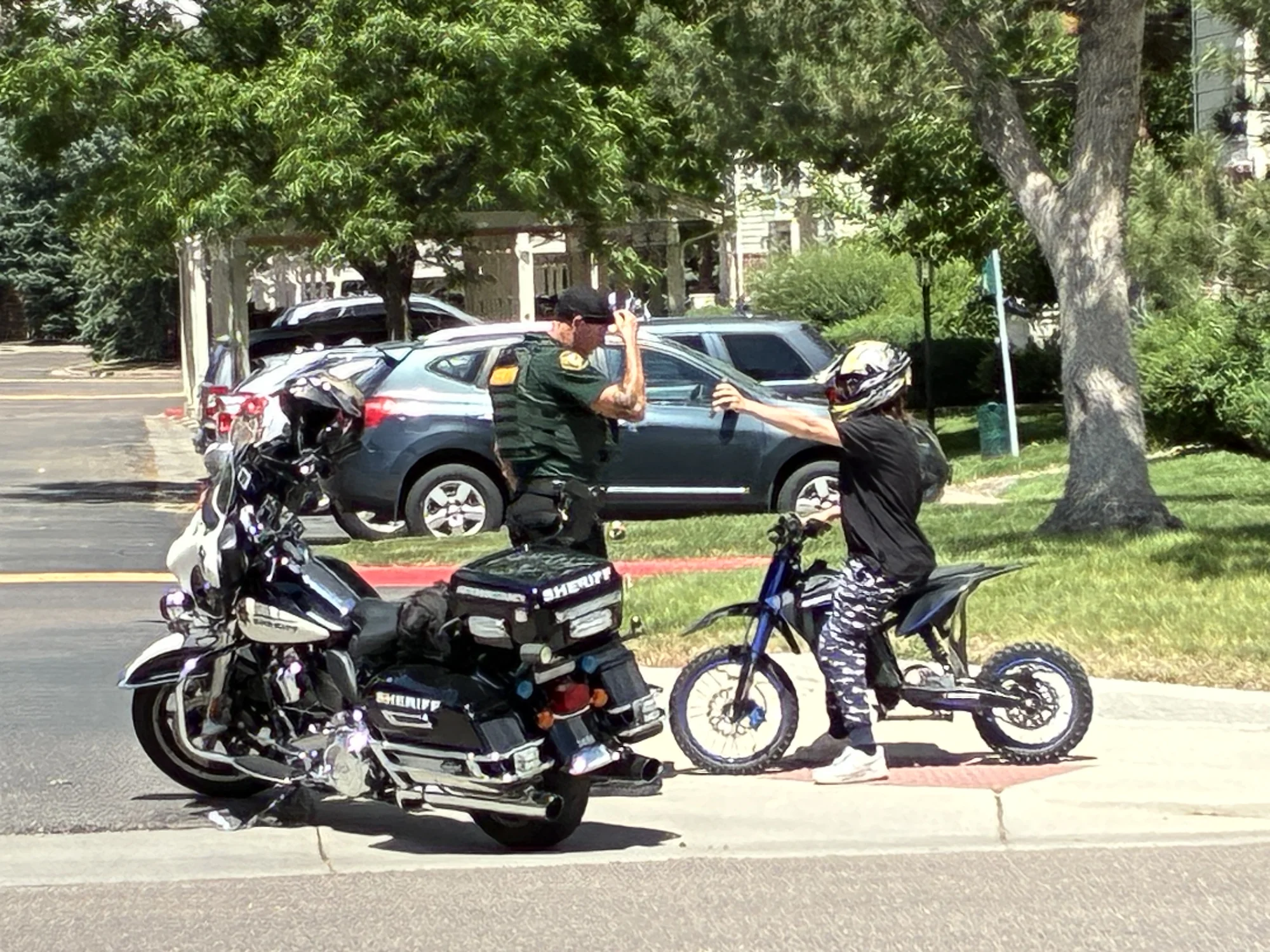 A JCSO motor deputy beside his patrol motorcycle talking with a helmeted young e-bike rider at the curb