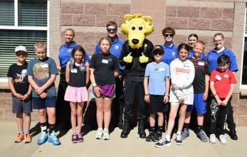 Elementary School Youth Academy students standing with deputies and a costumed mascot outside the academy building