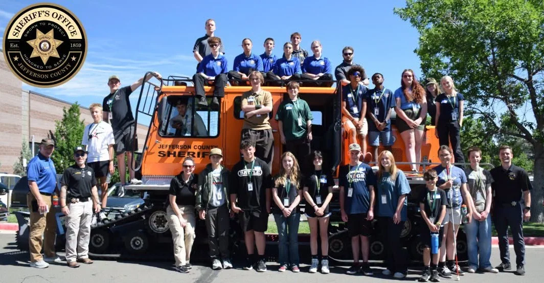 Youth Academy teens posing with deputies on and around an orange Jefferson County Sheriff snowcat