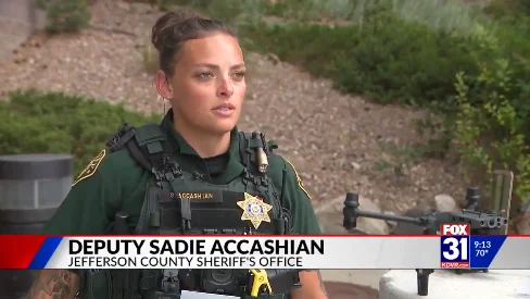 FOX31 news interview with JCSO drone operator Deputy Sadie Accashian, in uniform with a drone behind her; the on-screen caption reads "Deputy Sadie Accashian, Jefferson County Sheriff's Office"