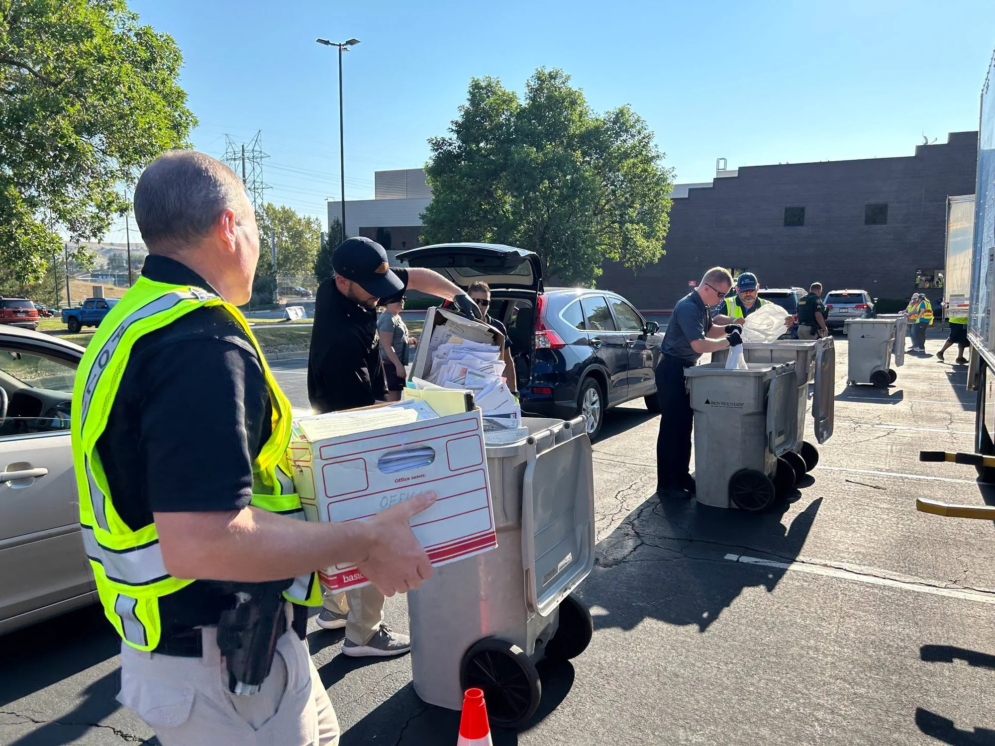 JCSO staff in safety vests unloading boxes of old paper records from cars into rolling shred bins in a parking lot during the Shred-A-Thon